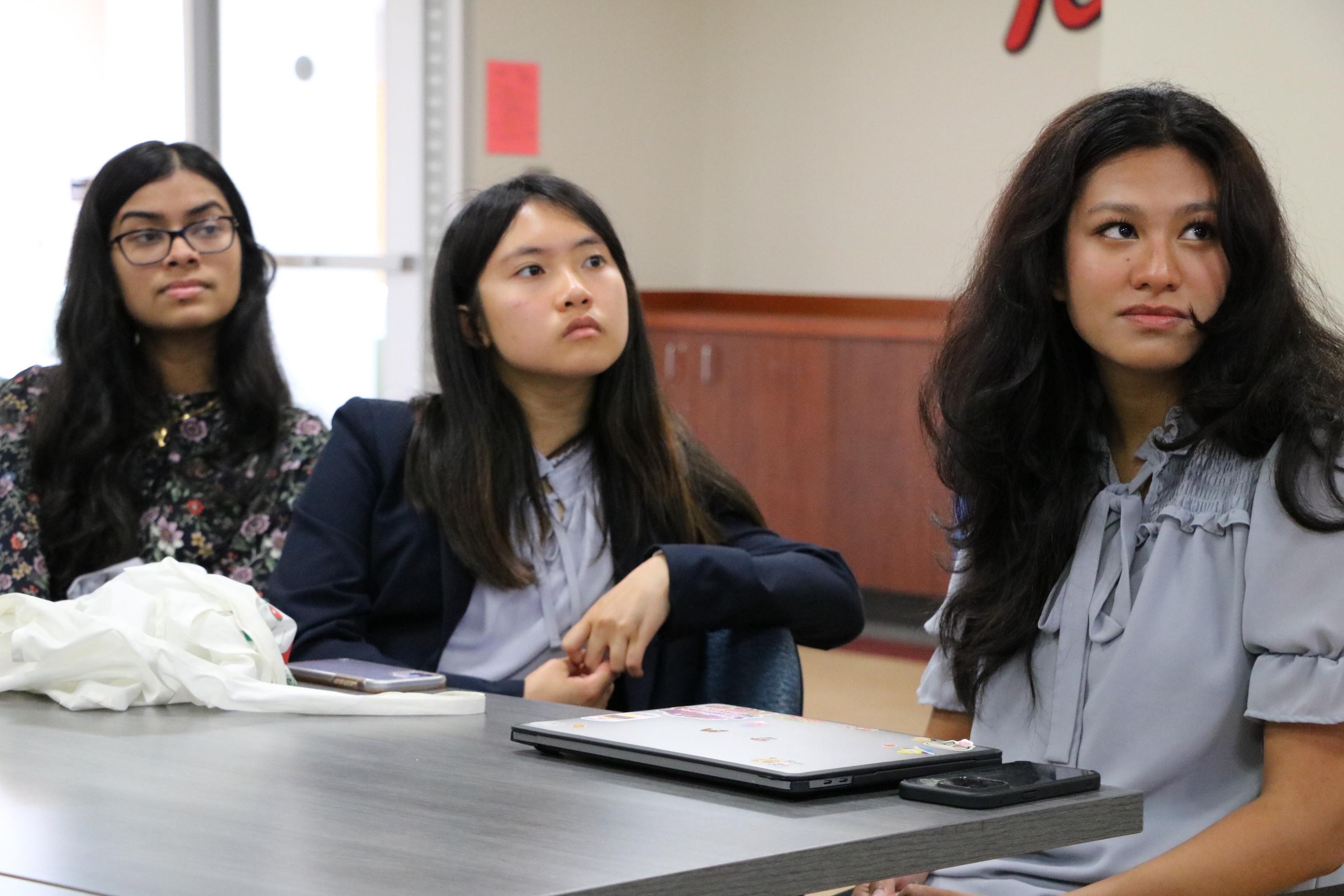 Three female students sit inside a classroom.