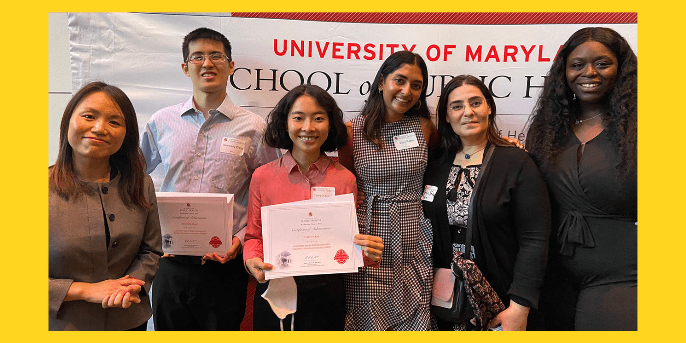 Faculty members and students stand in front of a University of Maryland sign.