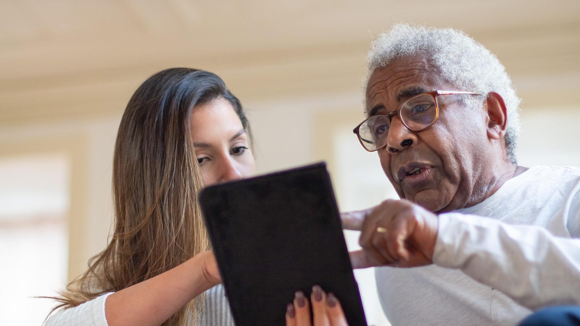 A woman holds a smart tablet as an older man points to the screen.