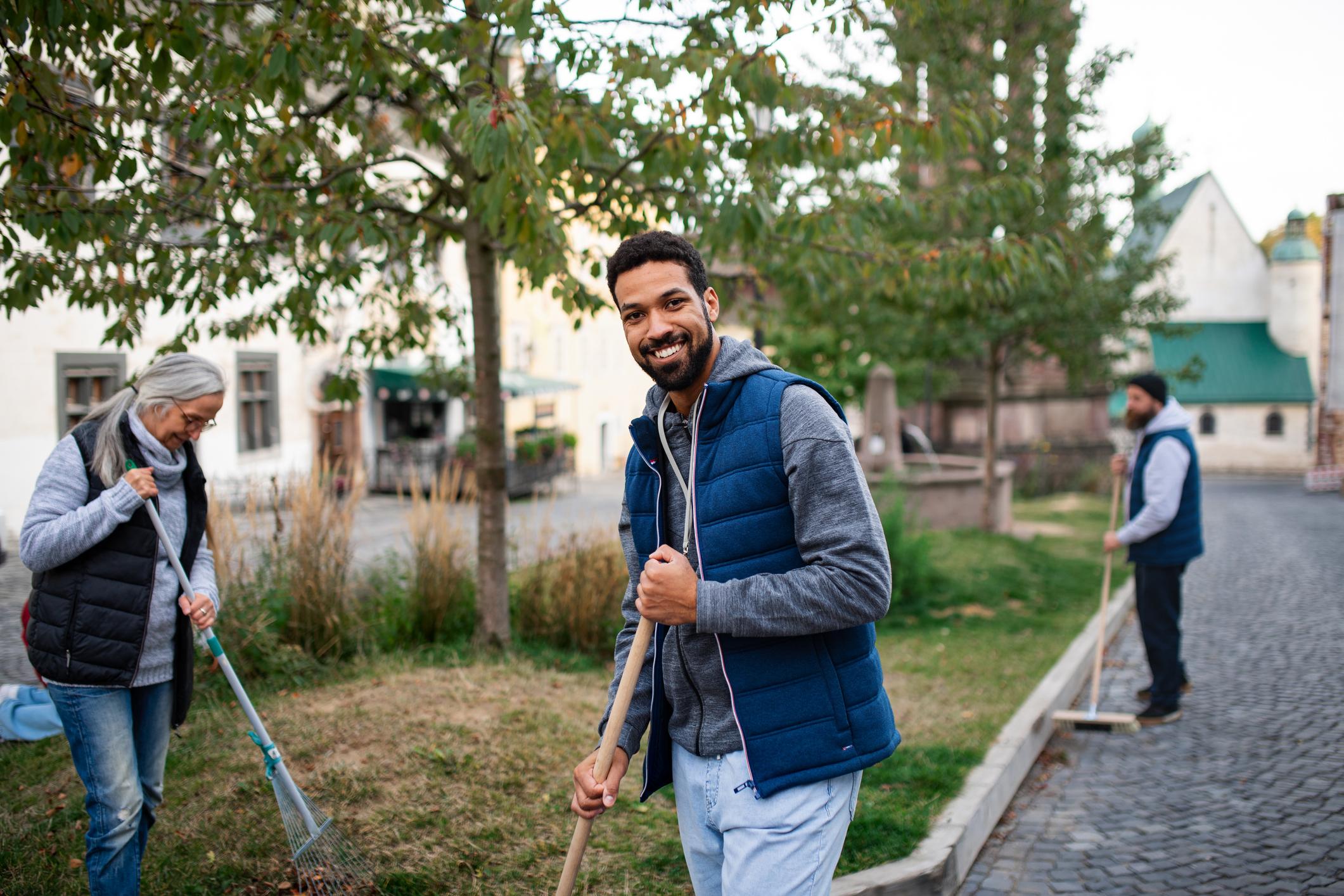 A young man volunteer with team looking at camera and cleaning up street.