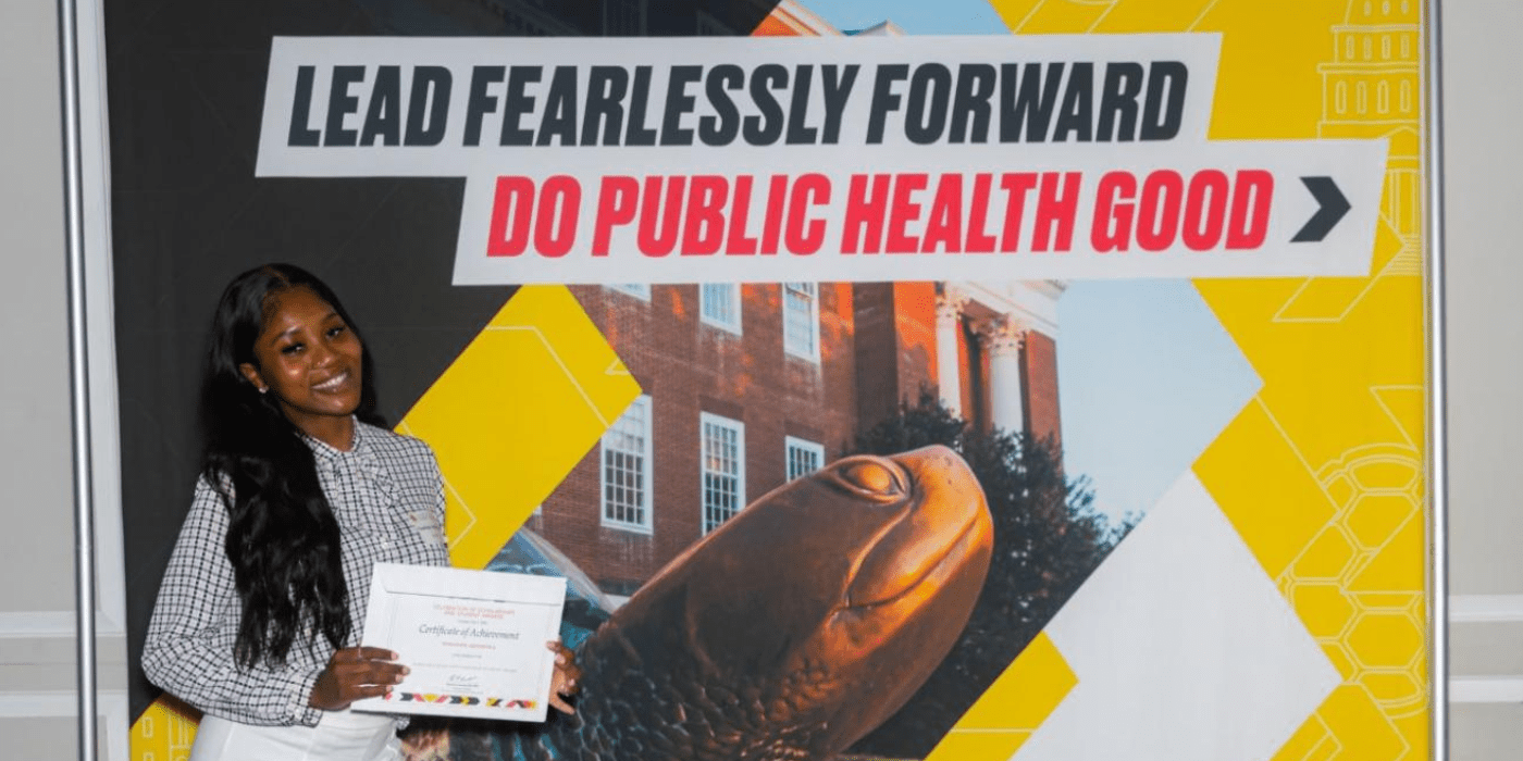 Smiling student stands in front of SPH banner that reads Do Public Health Good