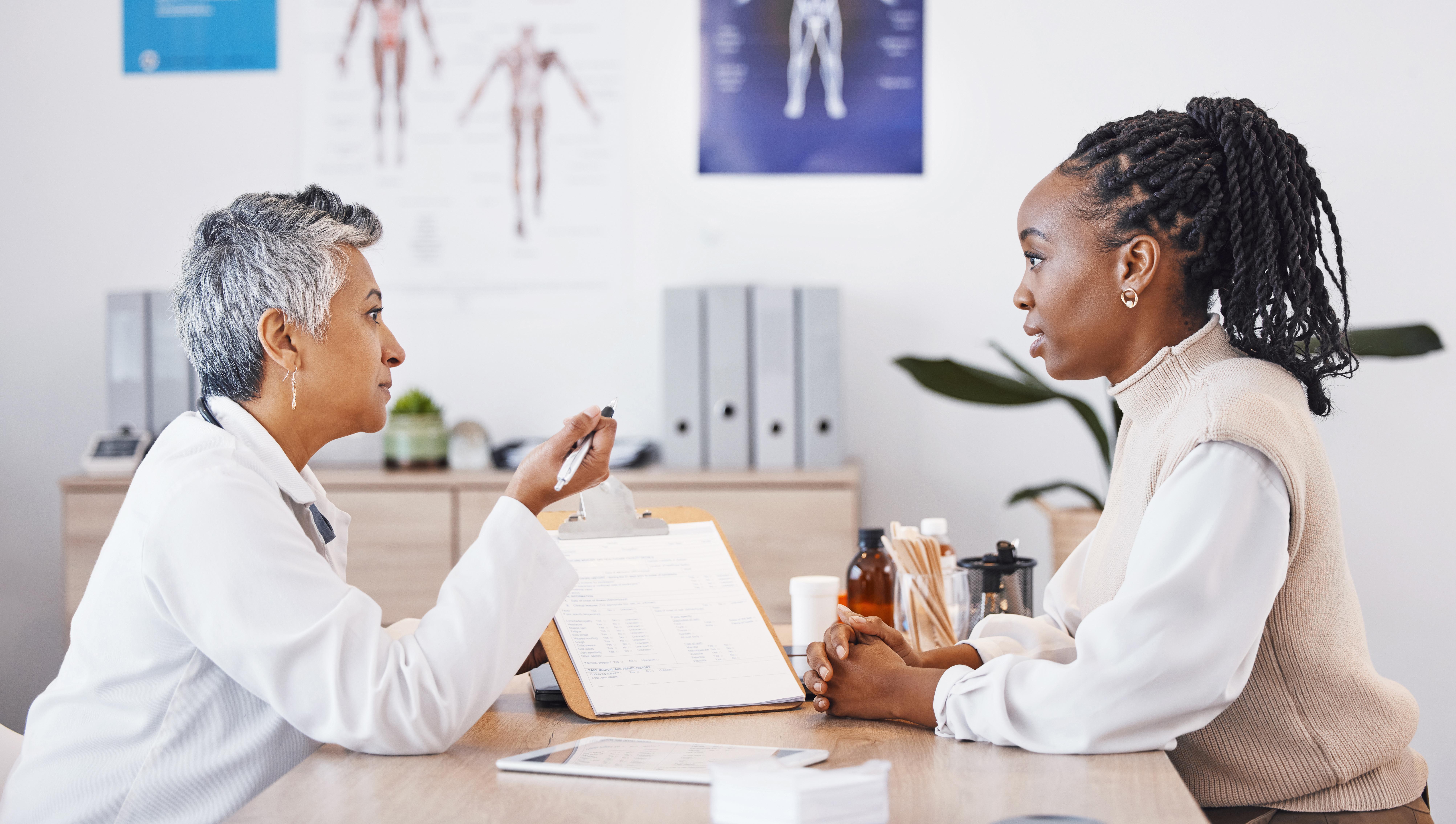 an Asian woman doctor speaks to a black woman patient