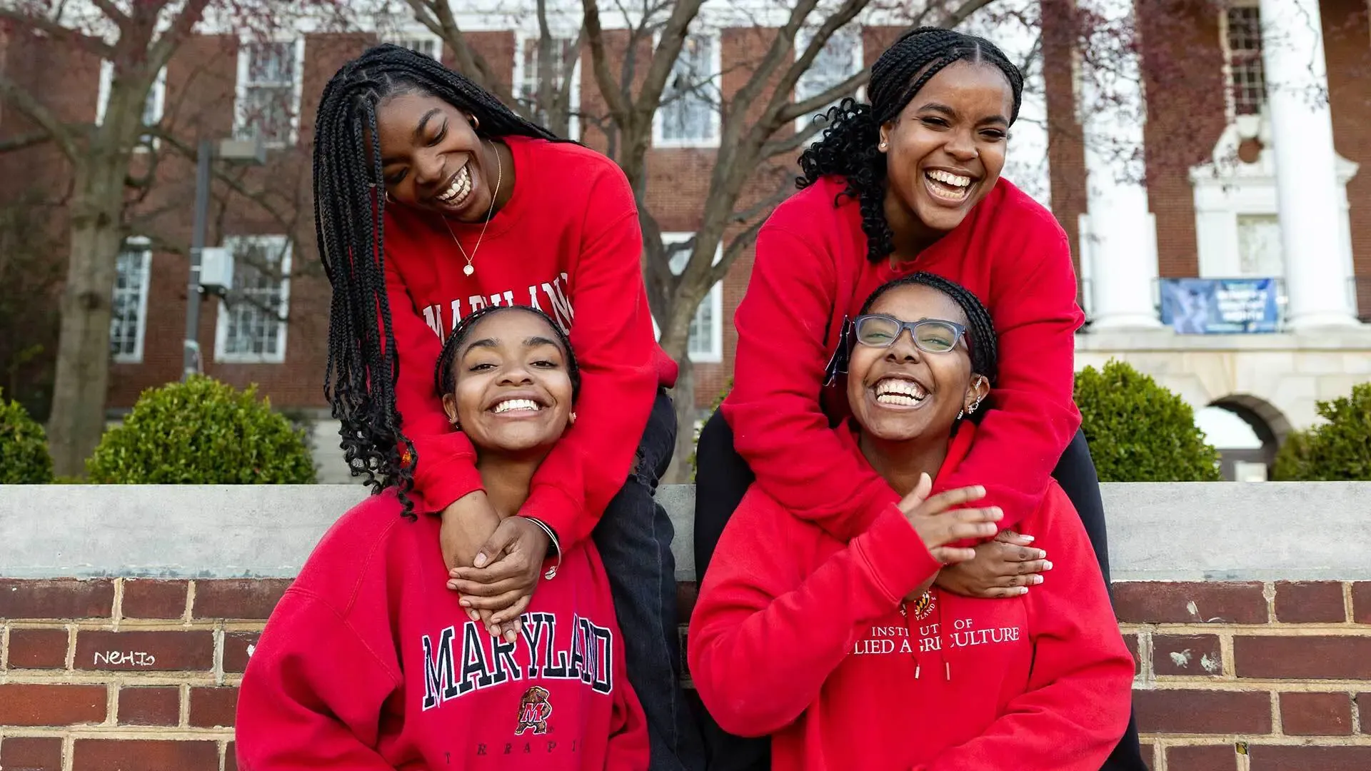 4 UMD students (that are also sisters) posed along brick wall in front of the Registrar building