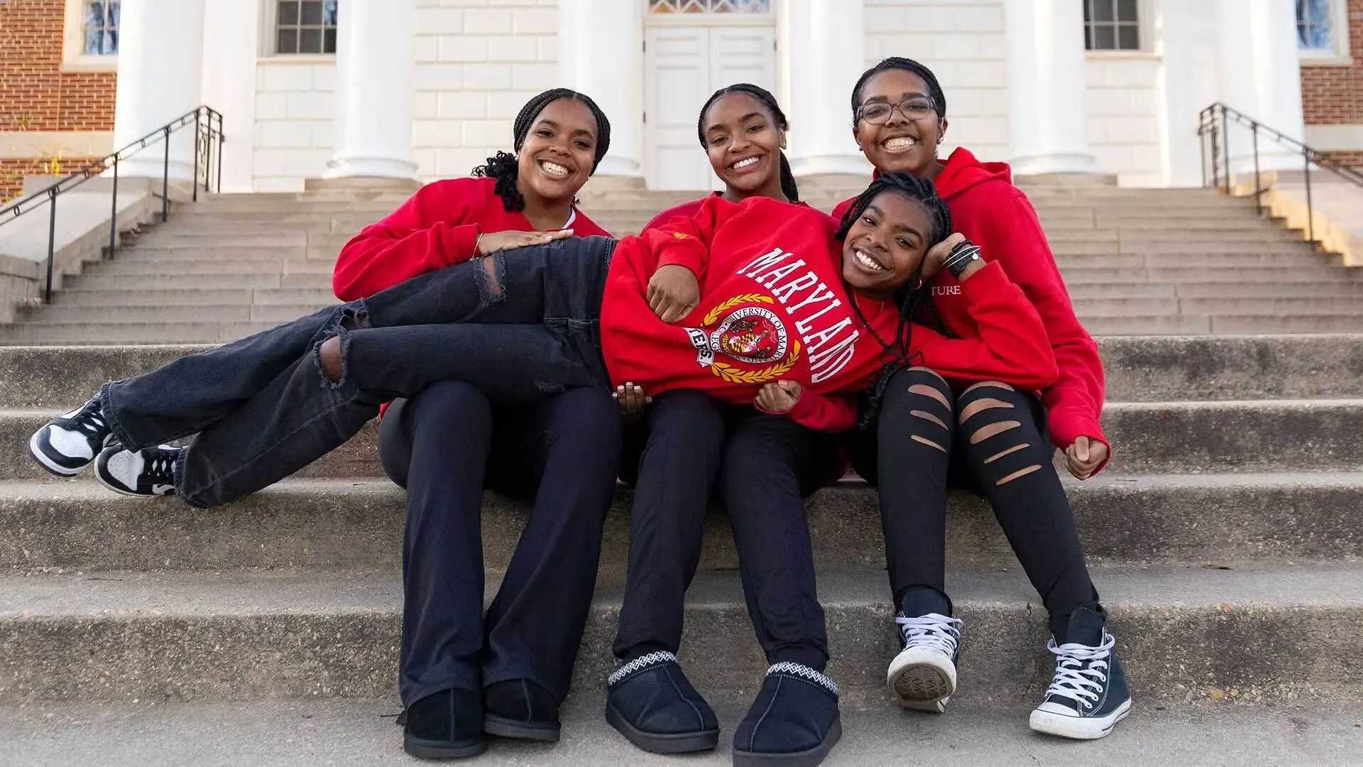 4 students sitting/laying along the steps in front of the Main Administration Building