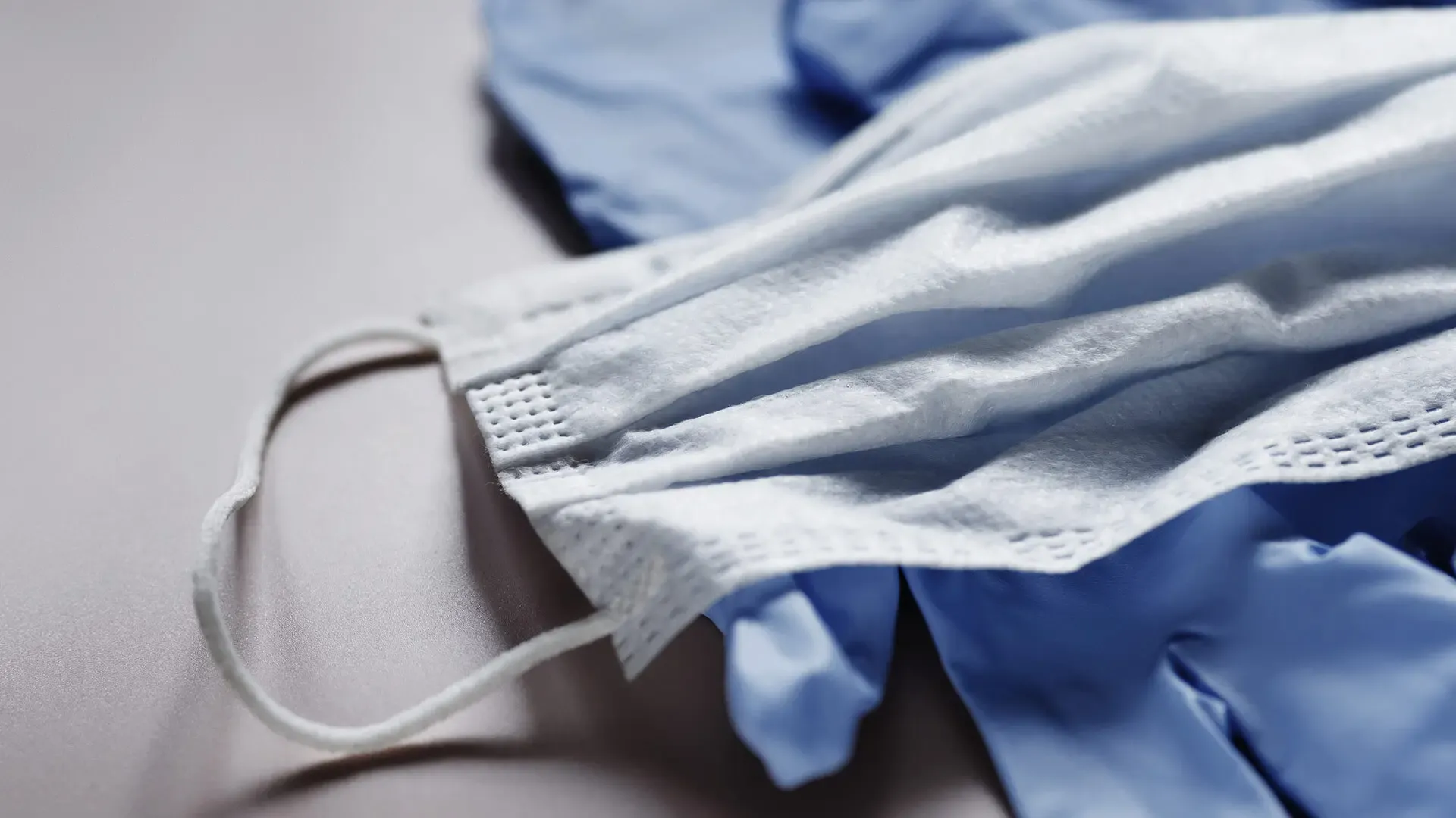 white background, focused on a blue glove under a n-95 mask