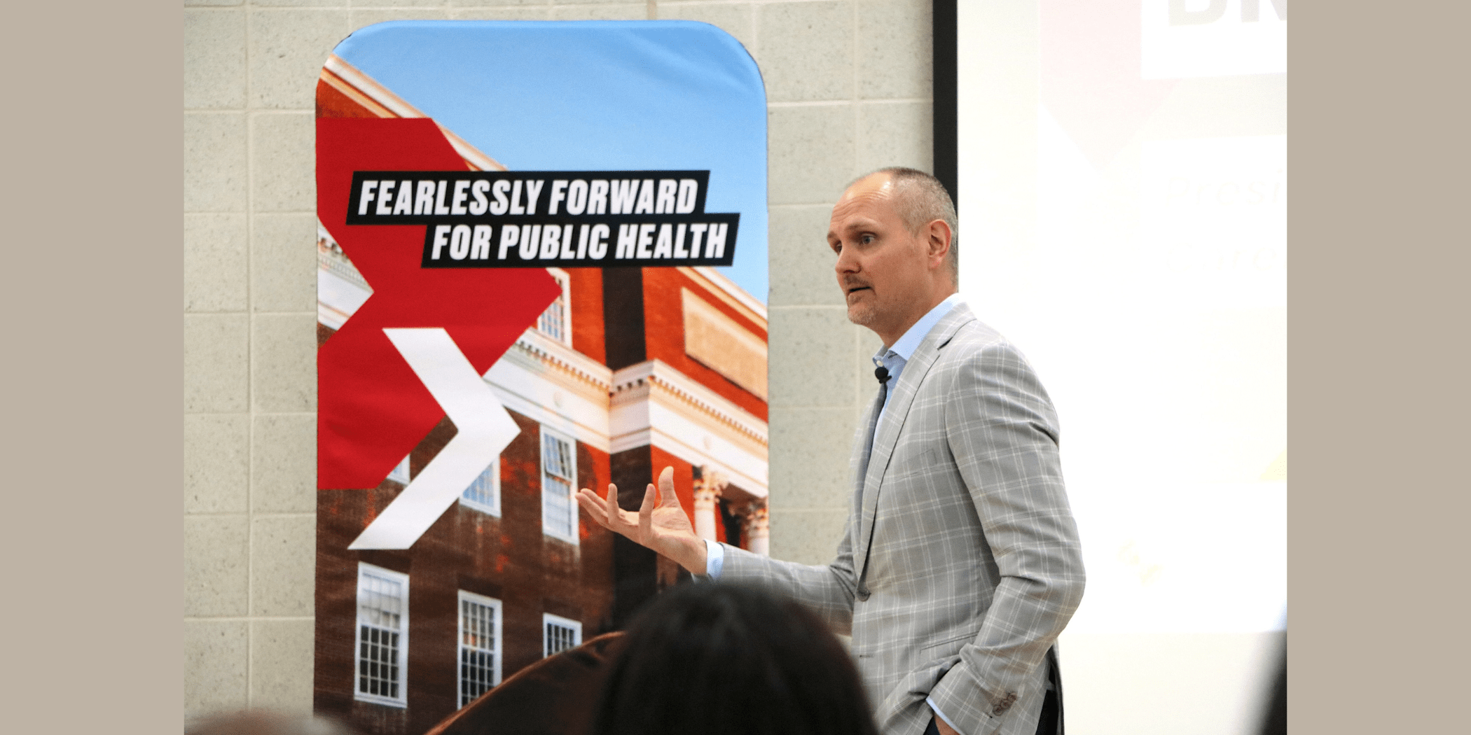 A man, Brian Pieninck, dressed in a grey suit delivering a speech at UMD