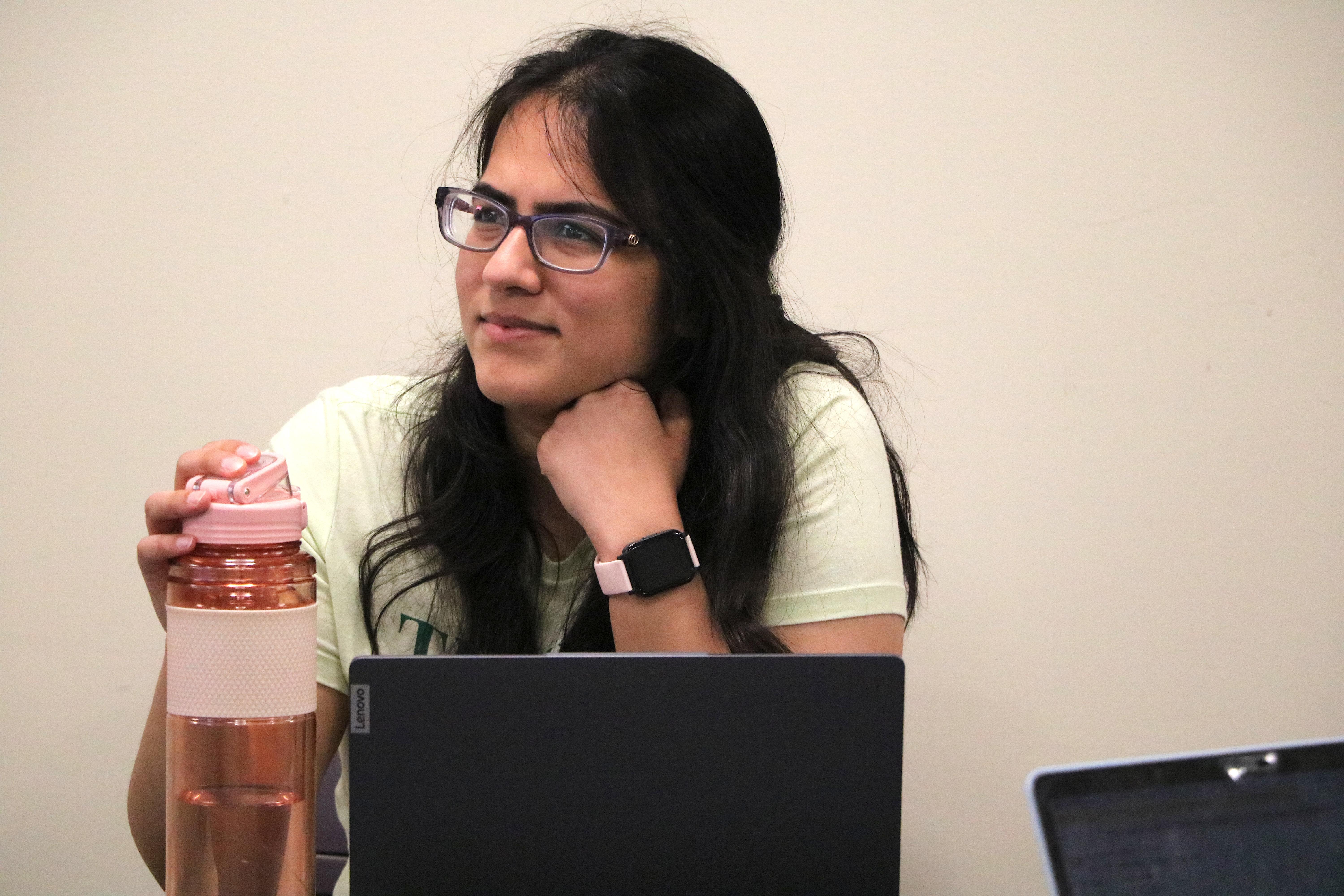 Student sits with laptop and water bottle smiling and concentrating