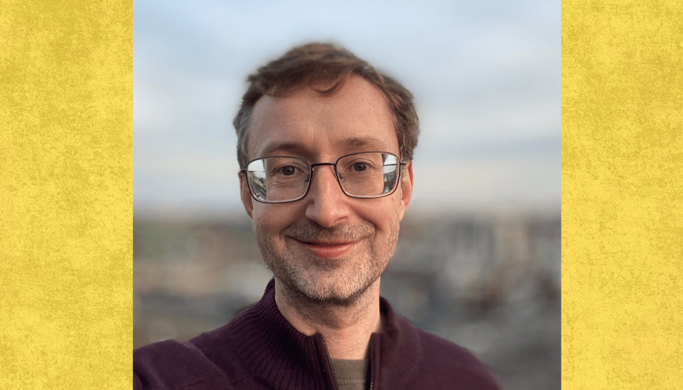 Professor smiles to camera with blurry cityscape behind him 