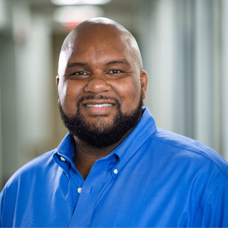 Black male professor wears blue button down smiles to camera