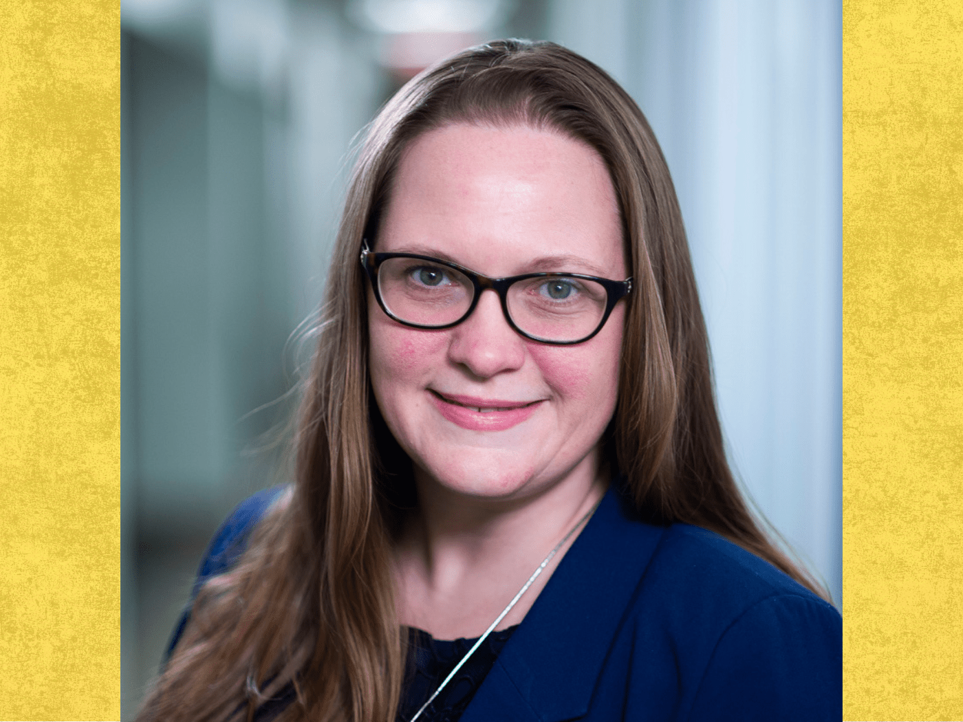 professor woman wearing navy top and glasses smiles to camera