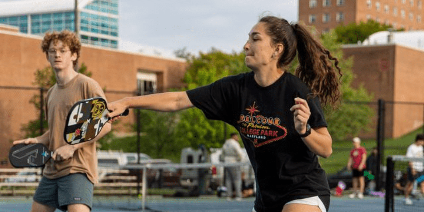 female student hits pickleball with paddle