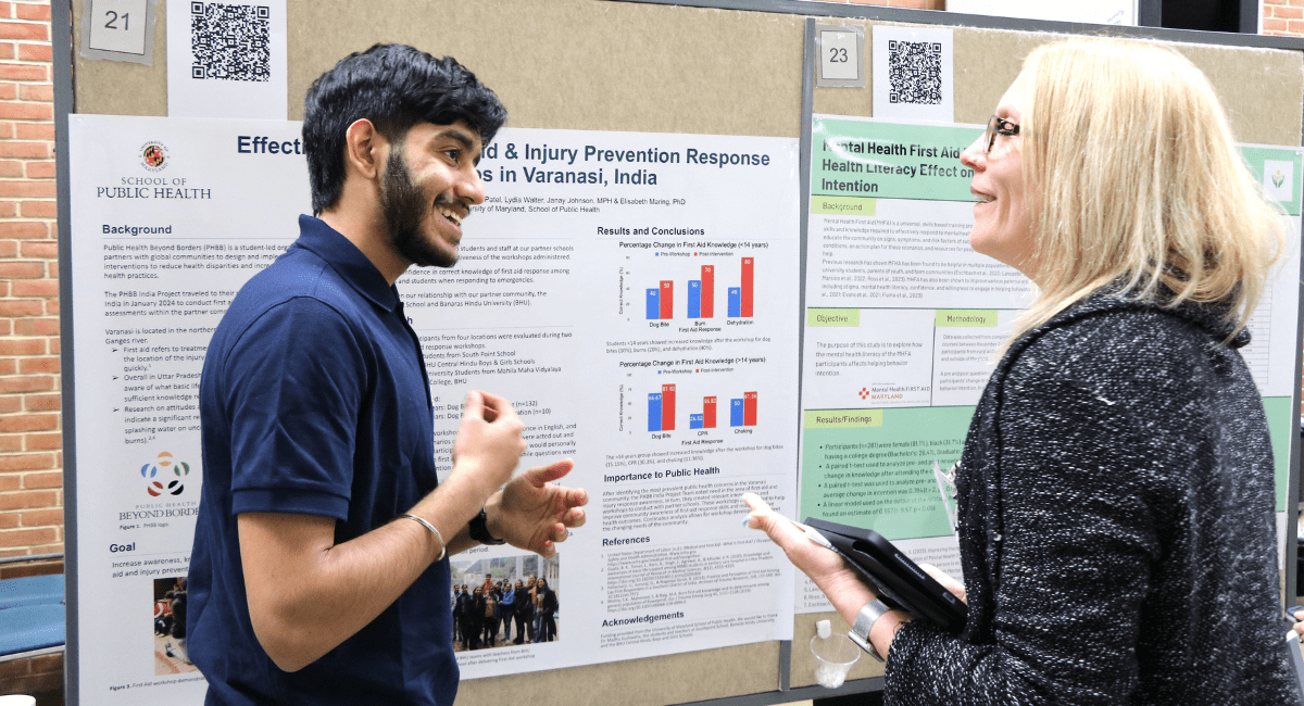 A University of Maryland School of Public Health student discusses a research poster on global health and injury prevention with a faculty member during a public health showcase.