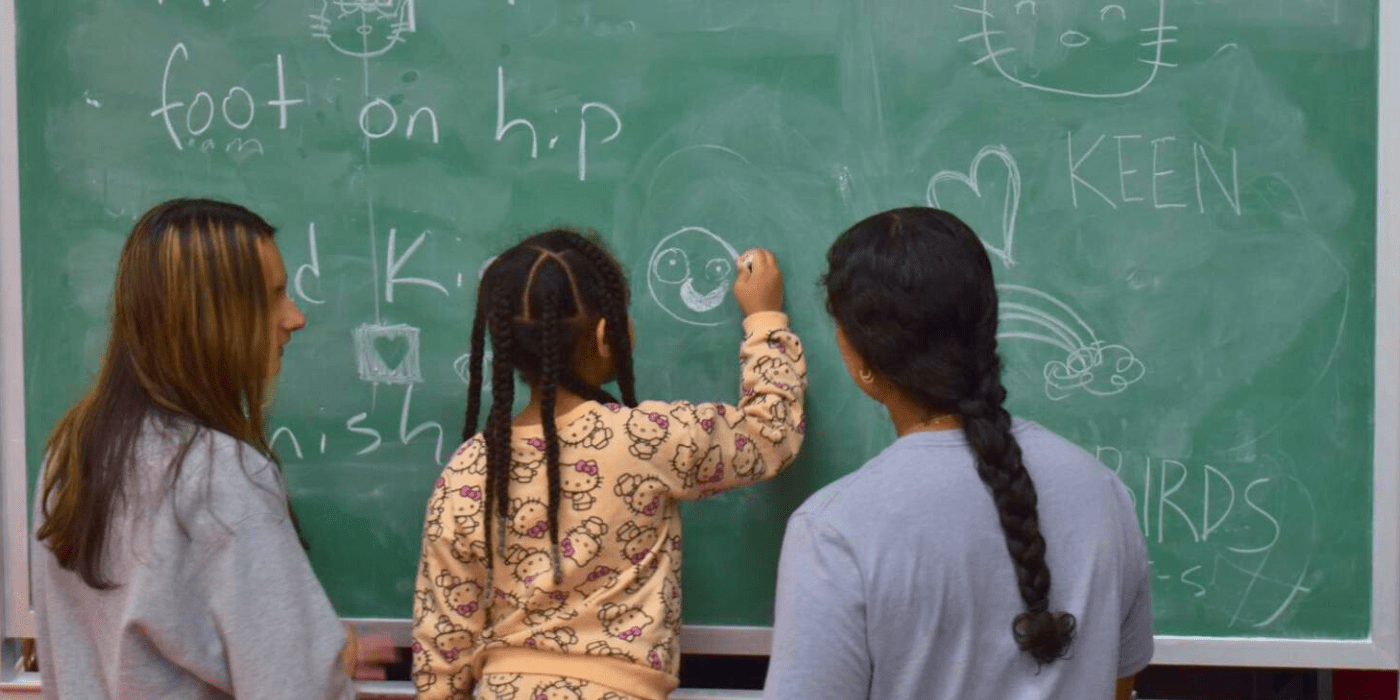 kid with two student volunteers draws a face on the greenboard