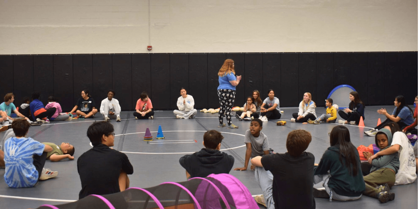 group of youth with disabilities sit in a circle with student volunteers in the gym