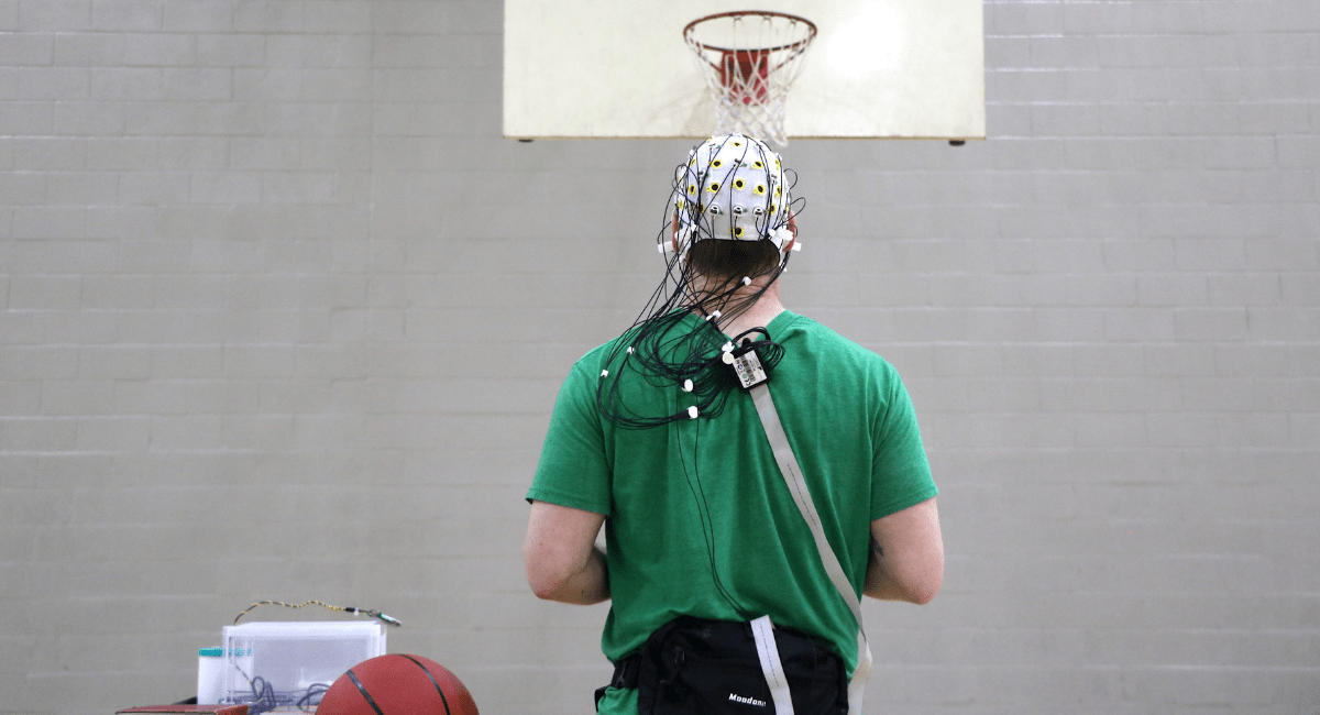 Man with wired brainwave cap on standing at a basketball free throw line