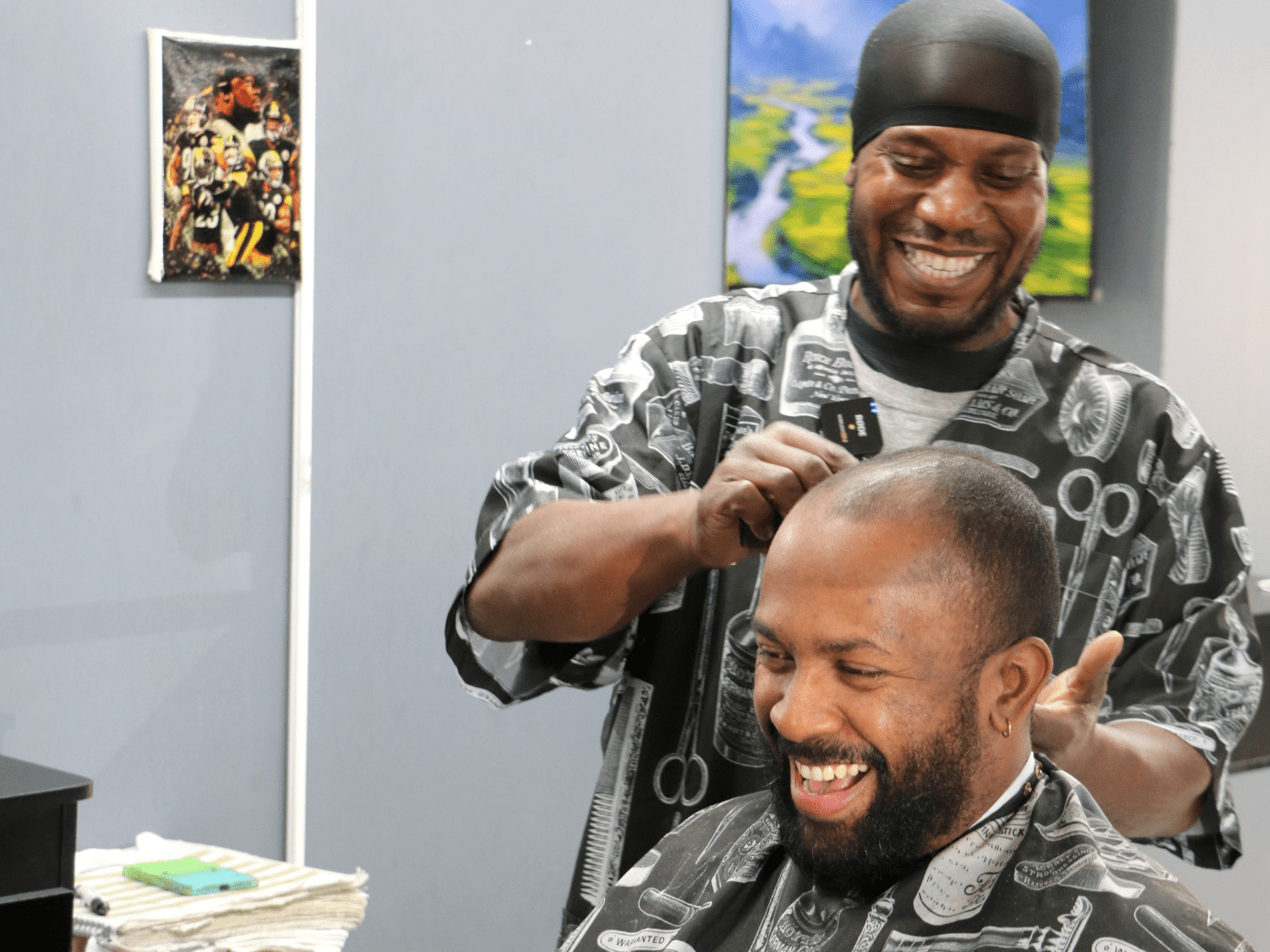 Black man barber makes a joke while his Black man customer laughs, sitting in chair