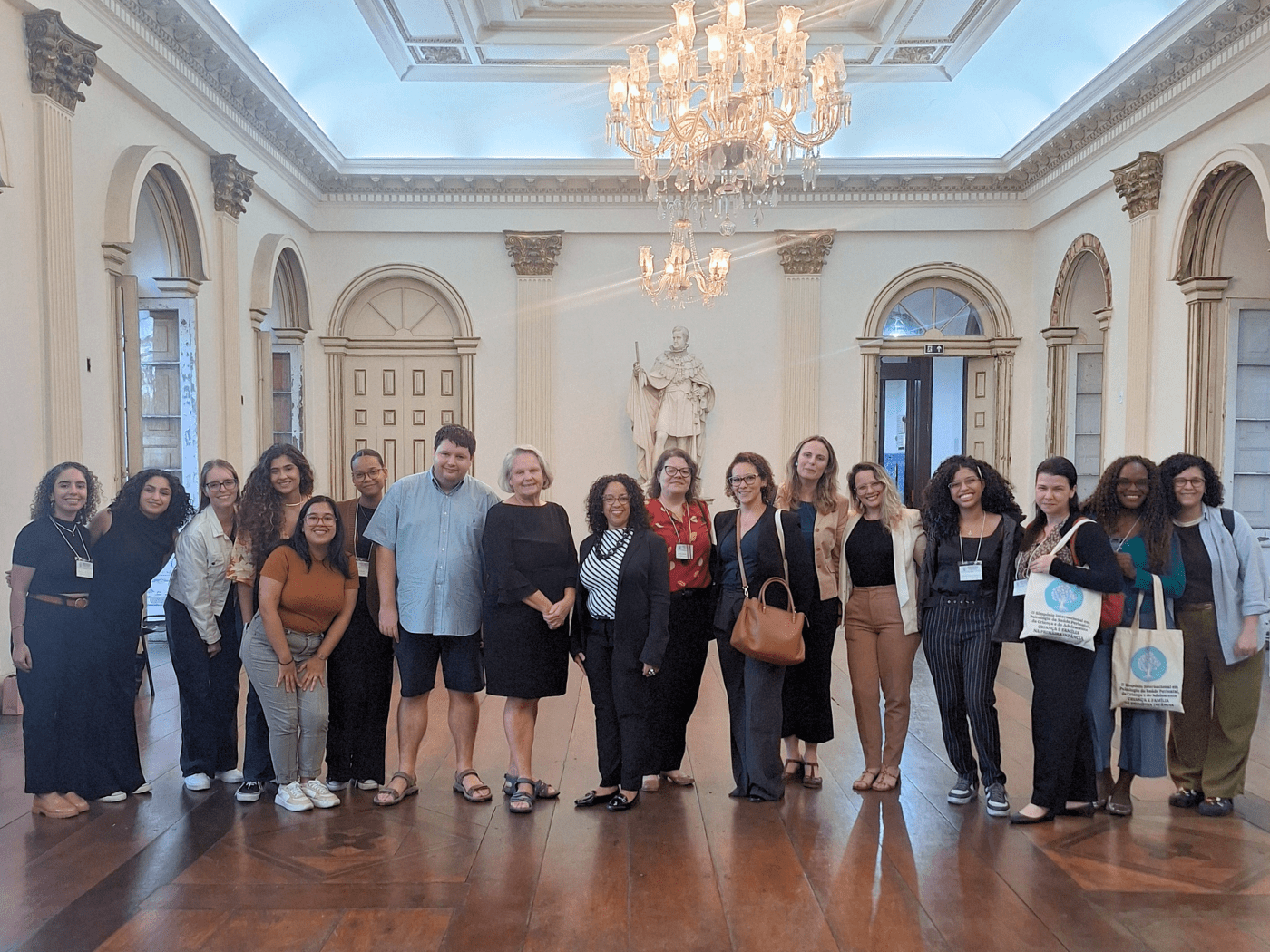 Group of students and faculty pose in a grand high ceilinged room with a chandelier