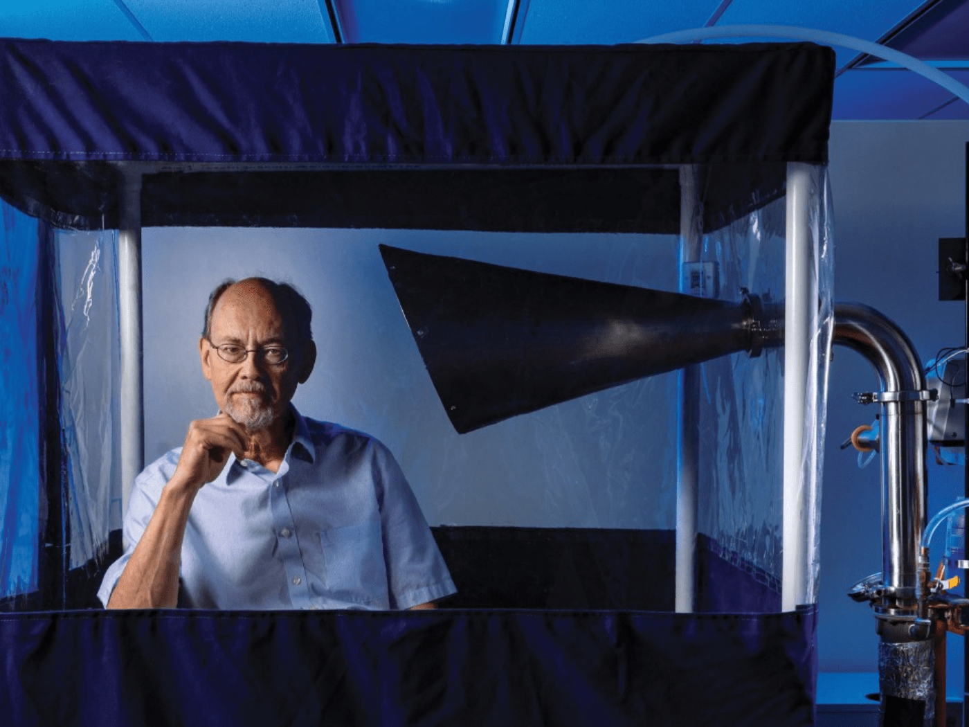 Professor sits inside his invention, the Gesundheit machine, looking at camera with hand to his chin