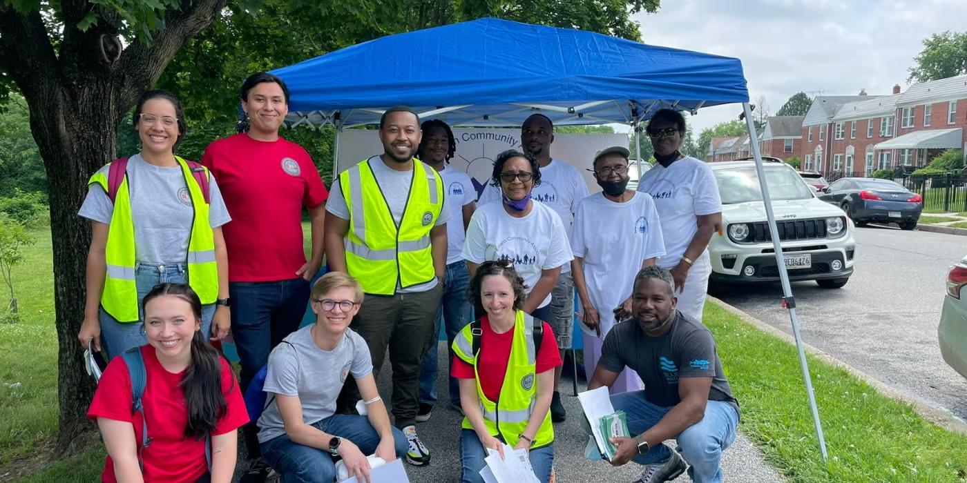 Group of volunteers posing under a blue canopy at a community outreach event.