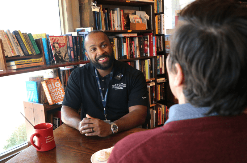 Man sitting at a table inside a library cafe with a black polo shirt on