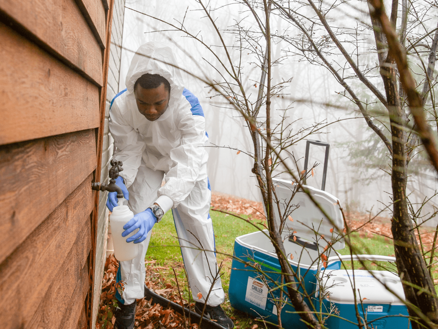 Black man researcher in hazmat suit collects water from an outside faucet