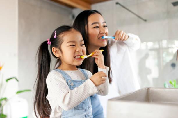 Little girl and mom brushing their teeth together in the bathroom
