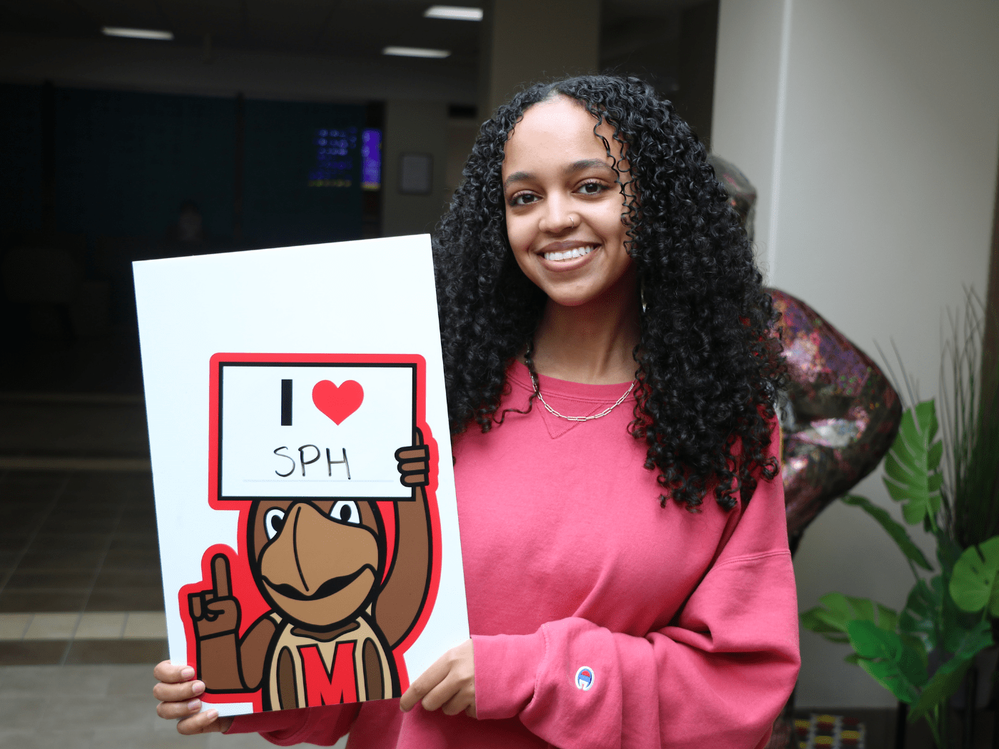 female student smiles to camera holding a sign that says I “heart” SPH