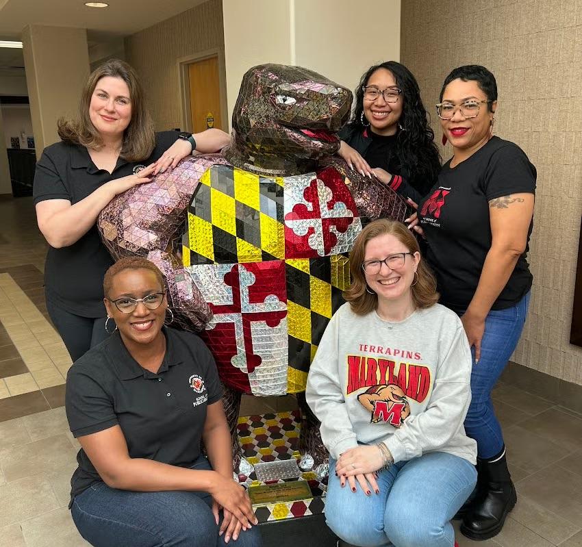 Five staff members pose with a mosaic University of Maryland Terrapin statue indoors.