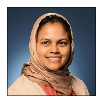 woman professor wearing beige headscarf and cardigan over pink top smiles to camera