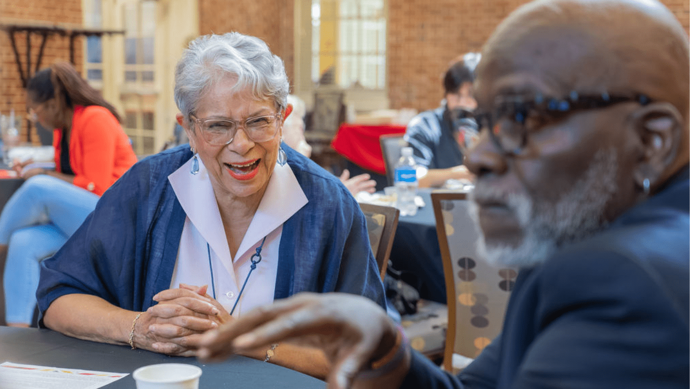 Two elder black people sit at a conference table talking