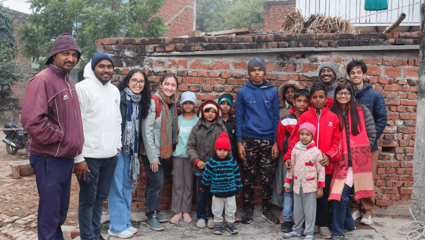Group of communities members in Varanasi stand with two UMD students in front of a brick building