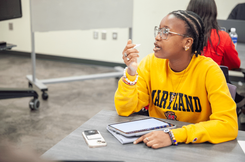 Student in a yellow Maryland sweatshirt sitting at a table in discussion