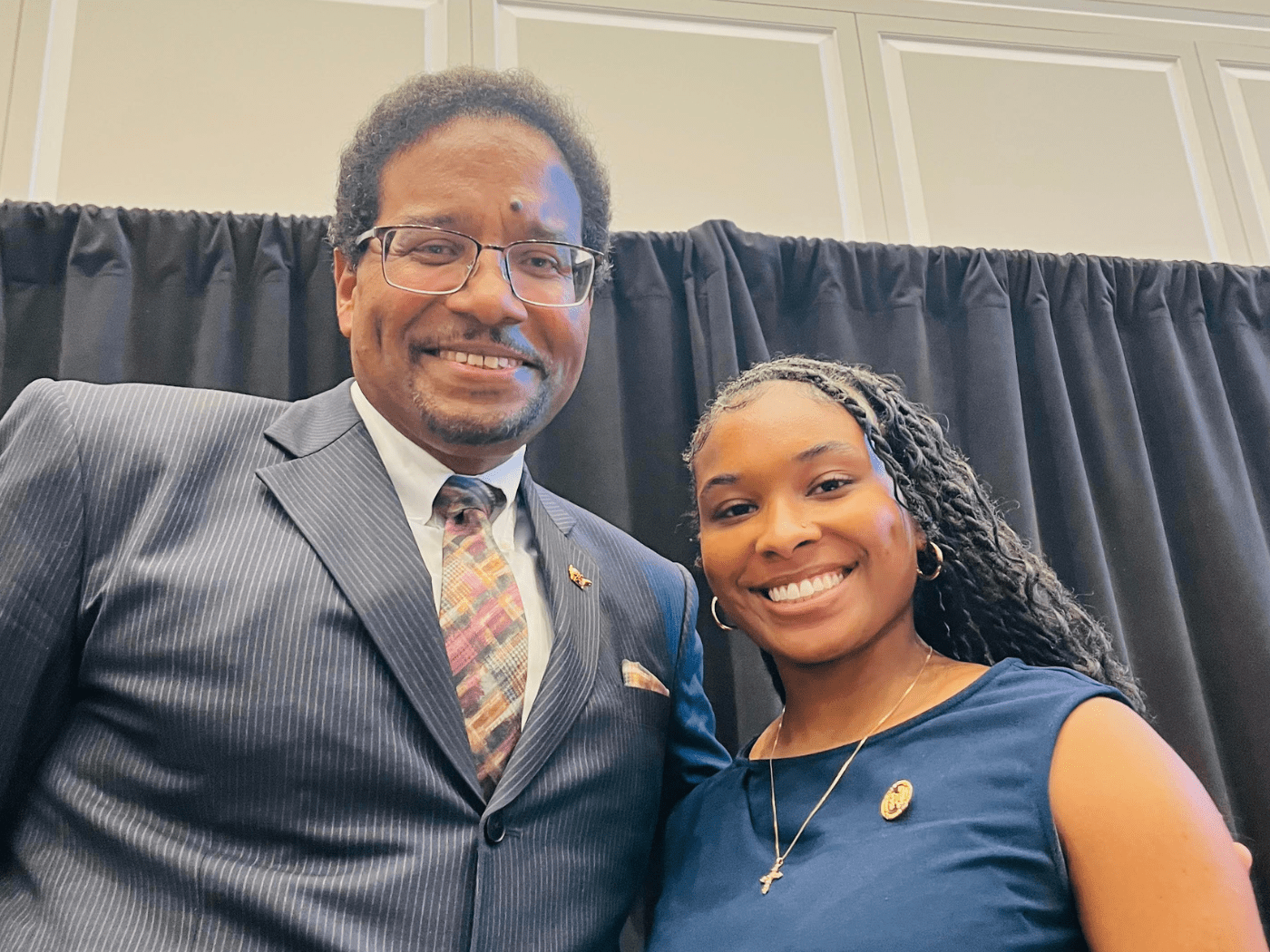 Black man in suit and young black student woman in teal top smile to camera