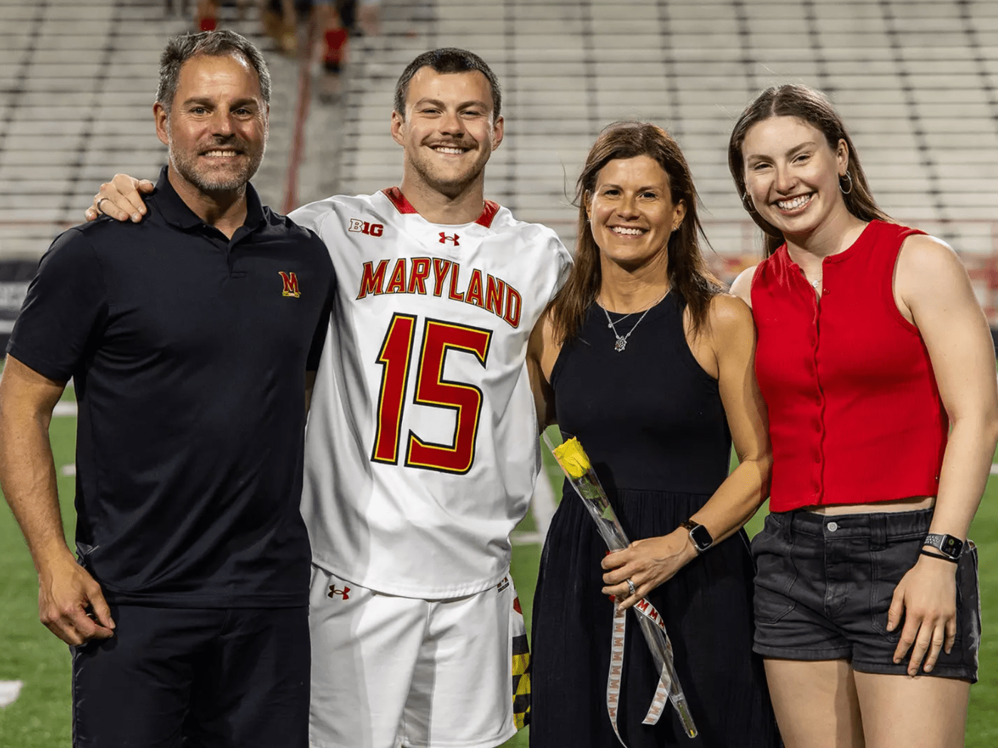 Young male athlete in Maryland athletic gear poses with mother, father, sister, with stadium bleachers in background