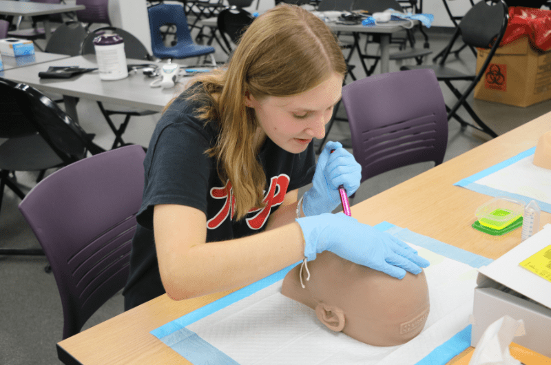 student practicing medical procedure on dummy in class
