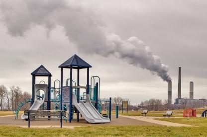 Playground With Factory Smokestack Billowing Pollution In The Background