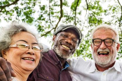 Three smiling older people outside with trees in the background