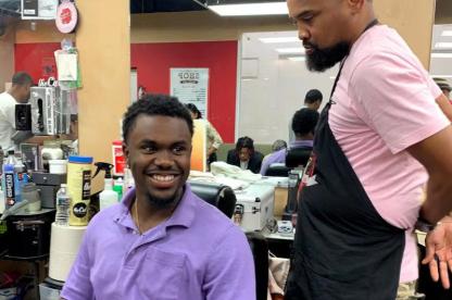 Barber stands beside a smiling customer seated in a barbershop chair.