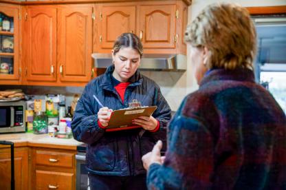 Female student taking notes on a clipboard while talking with another female adult