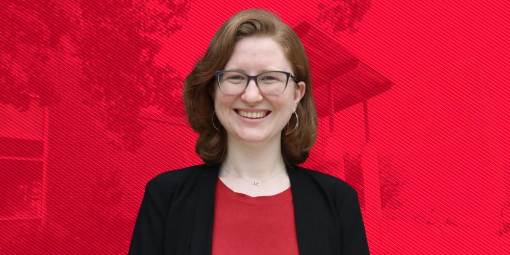 Smiling person wearing glasses stands in front of red background.