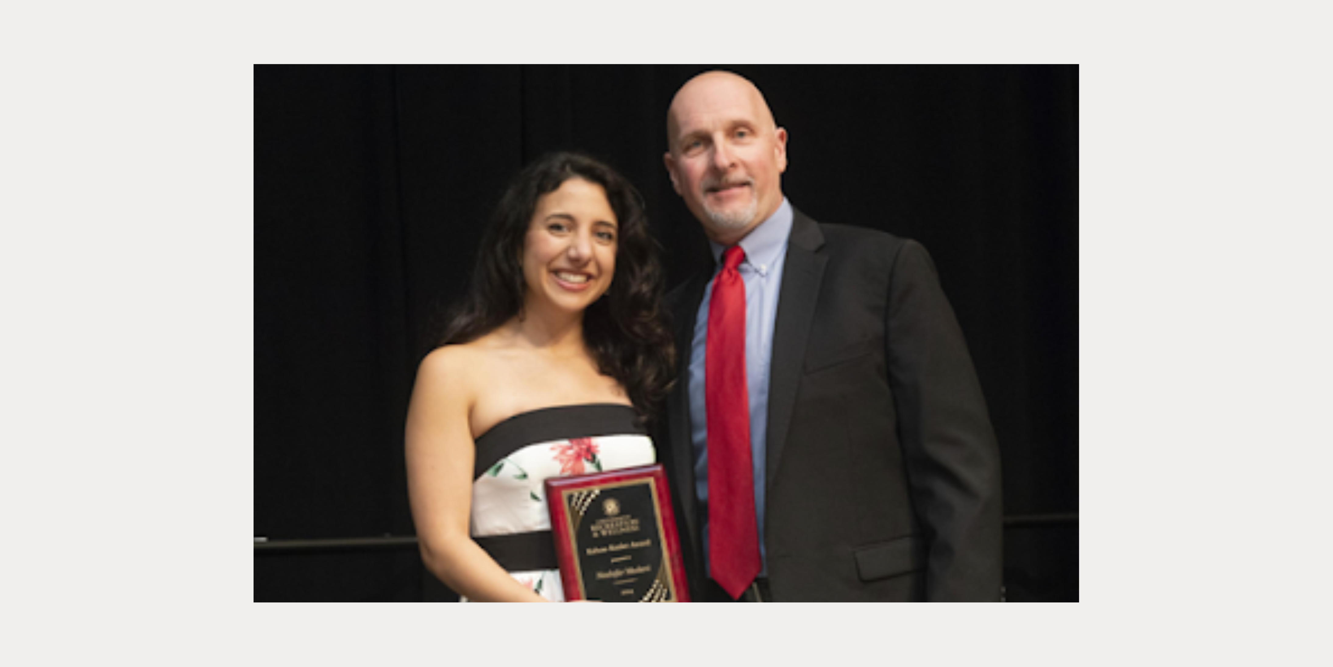 Woman student smiles as she poses with award with man in a suit. 